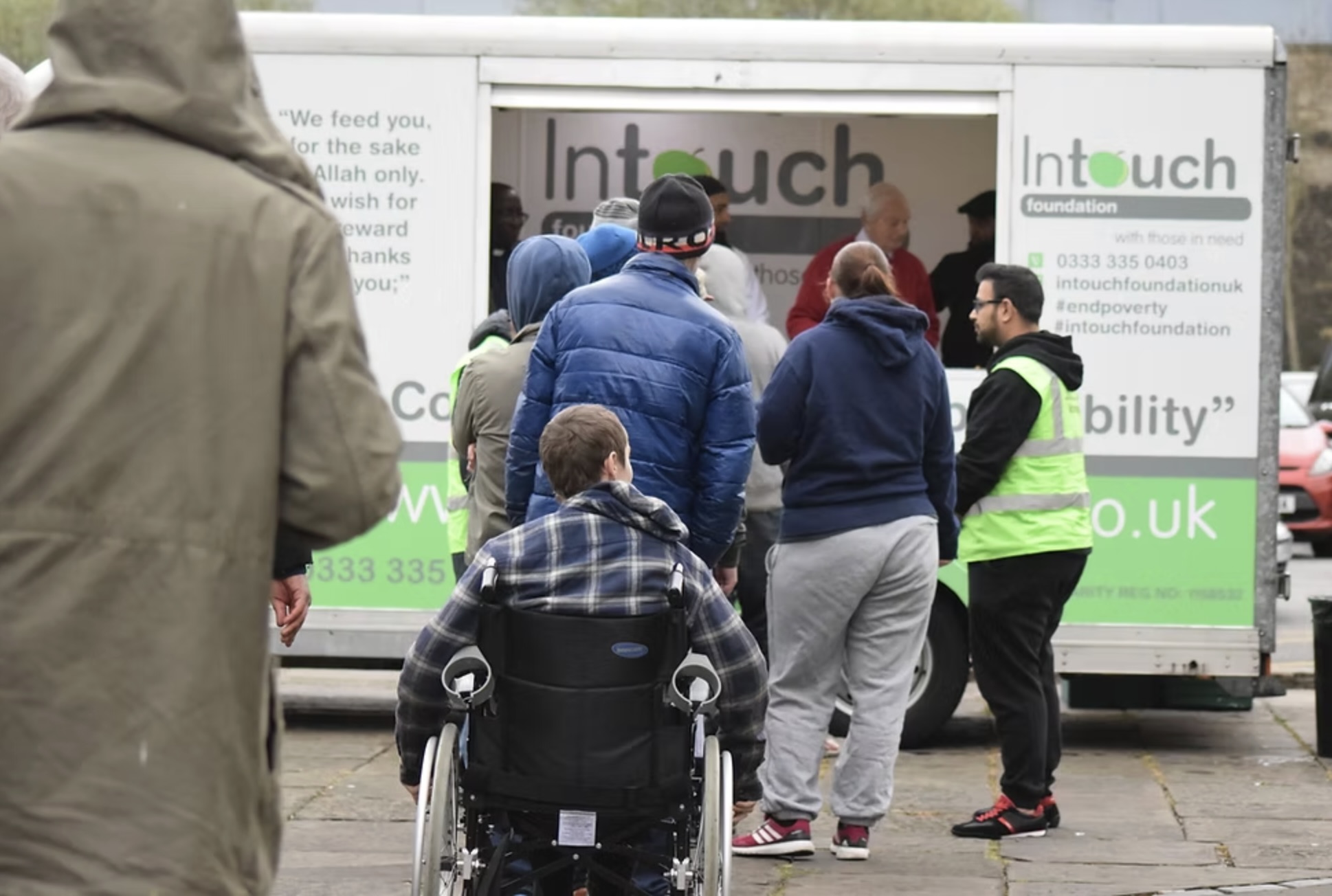 The image of people waiting a line in front of a mobile kitchen to collect food
